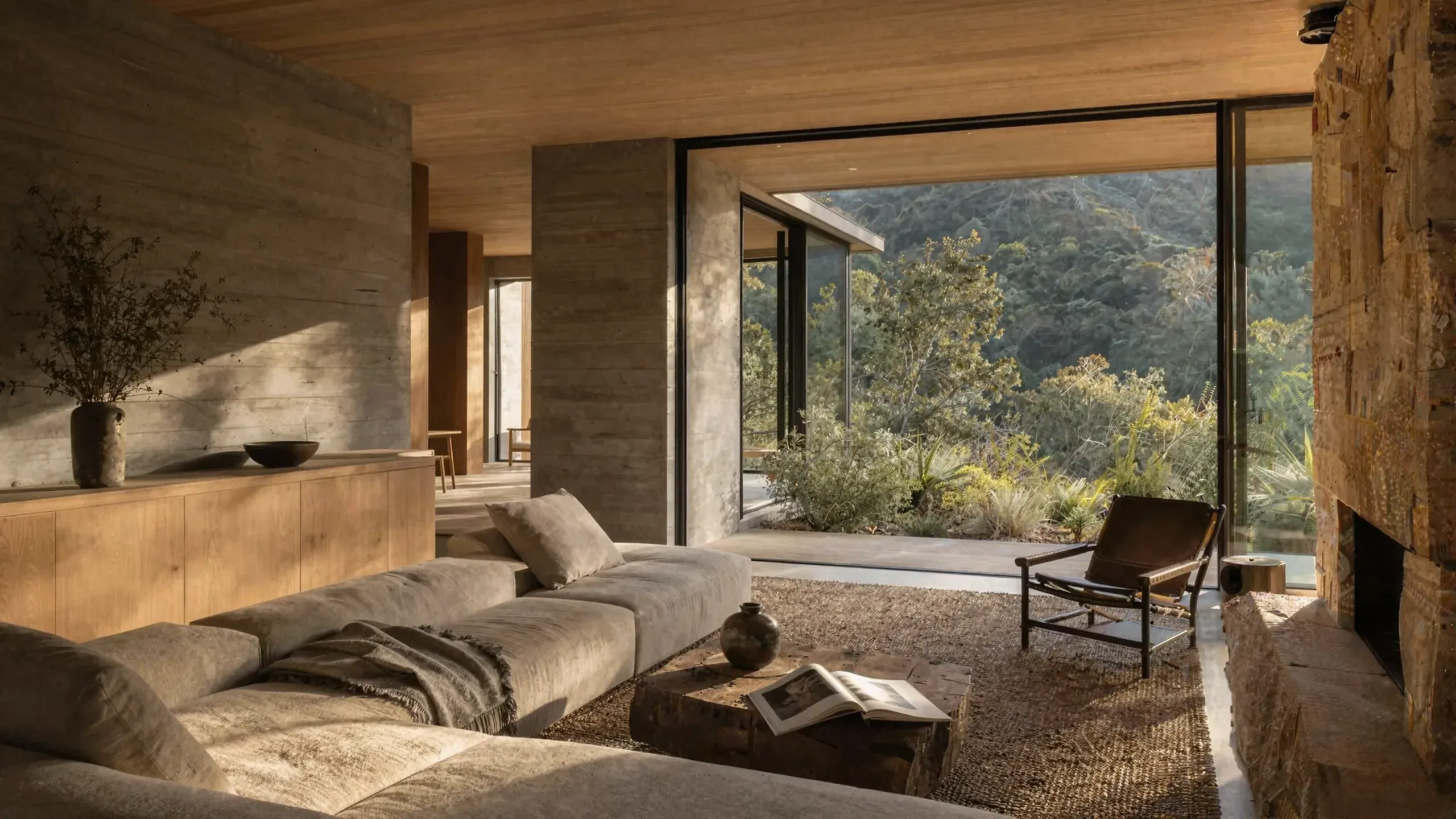 The living room: a low linen sofa, a lounge chair and a glass wall onto the canyon garden