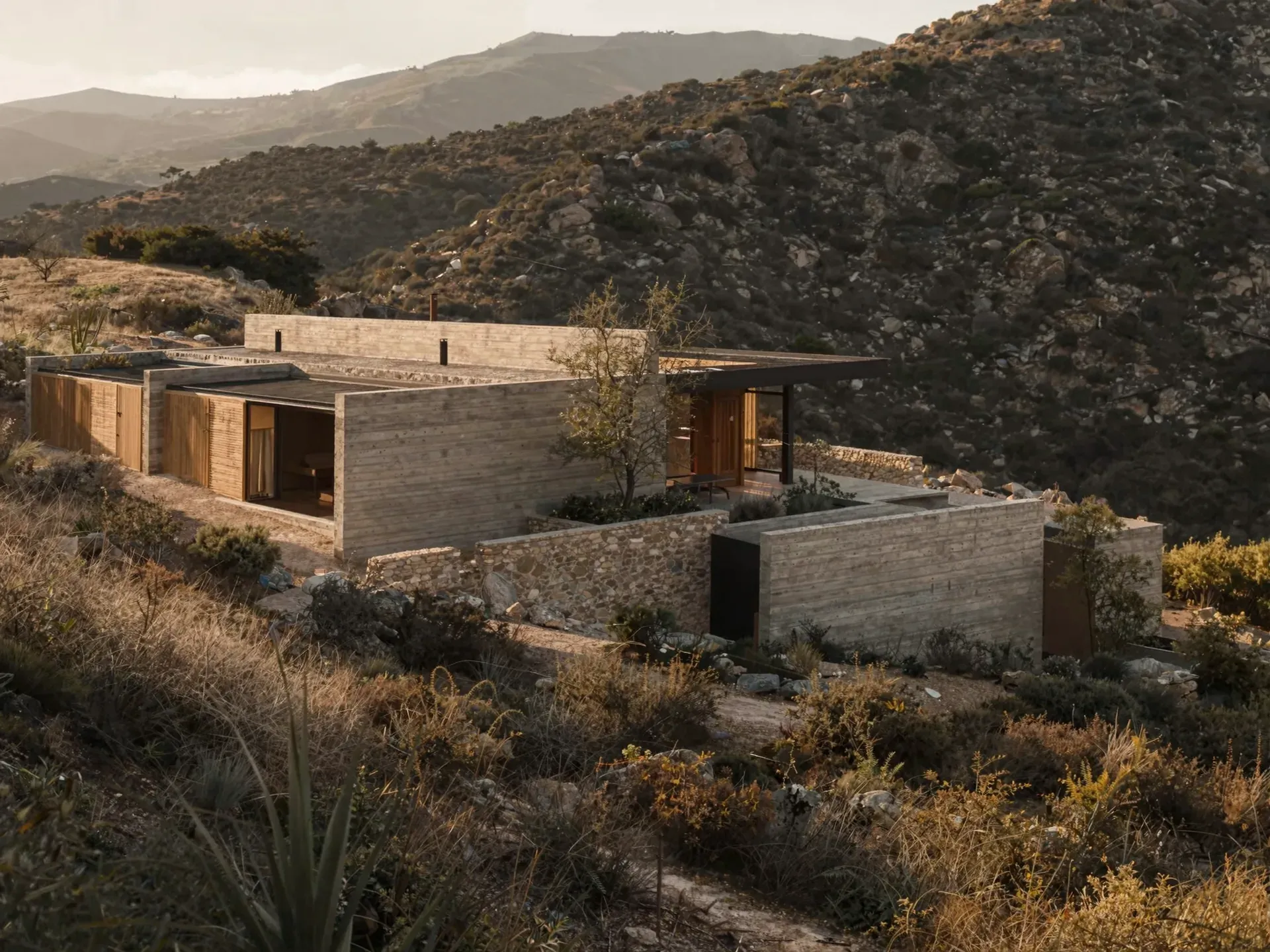 Aerial view of a low concrete and stone house on a chaparral hillside